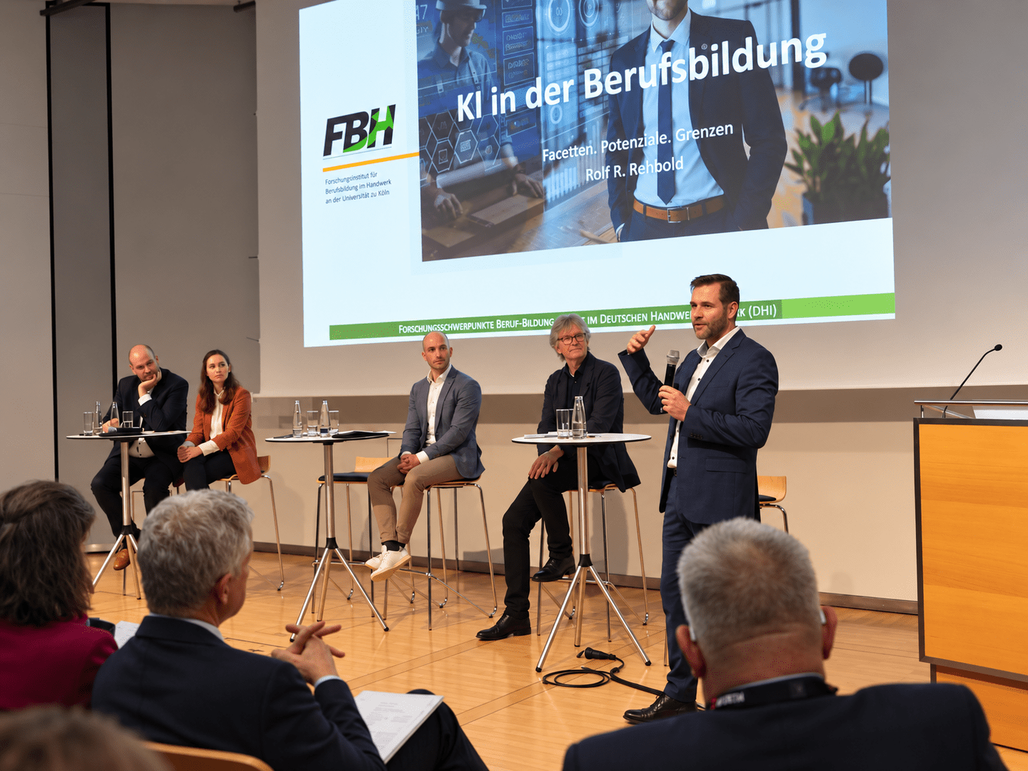 Rolf Rehbold spricht auf einem Podium zum Thema KI in der Berufsbildung, im Hintergrund das Logo des Forschungsinstituts fuer Berufsbildung im Handwerk (FBH) der Universitaet zu Koeln